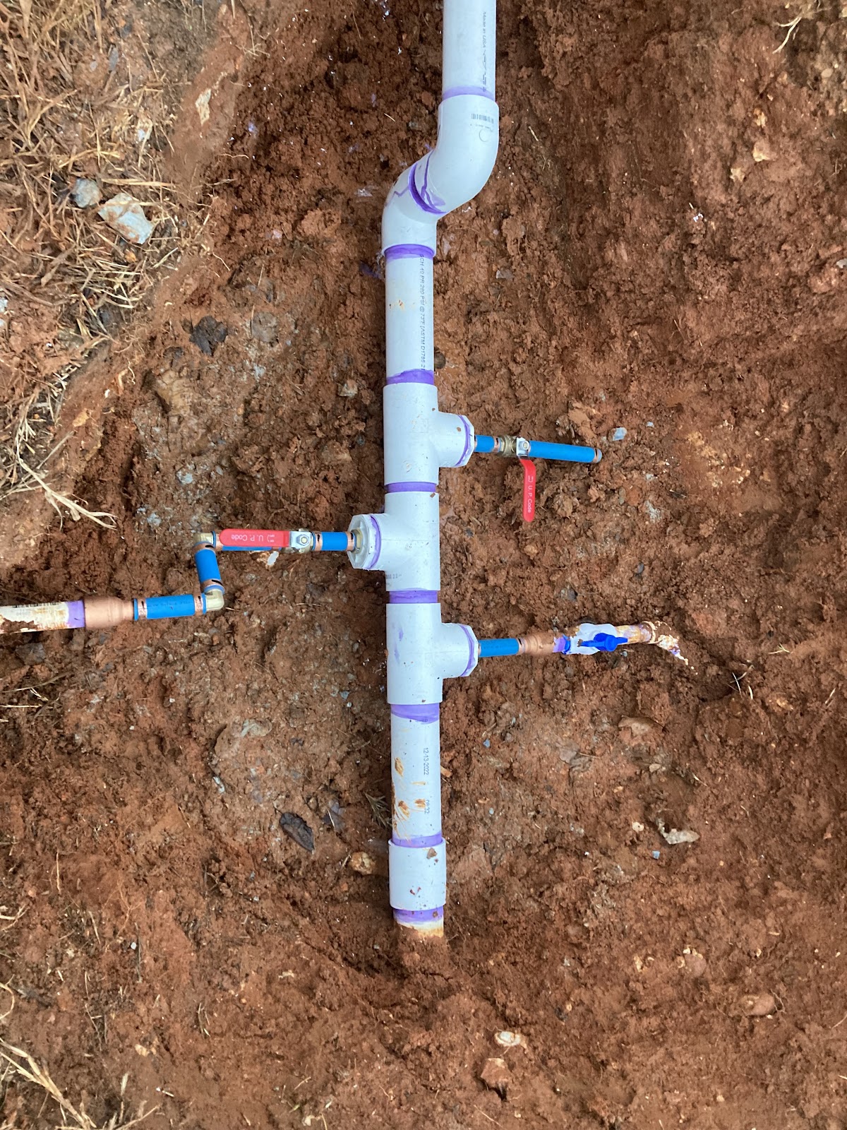 Underground PVC water line manifold in a red clay trench